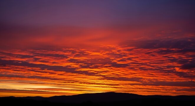 Fiery sunset sky with dramatic clouds. Vibrant orange and purple twilight over a mountain silhouette. Scenic nature landscape for travel and inspirational concepts - Powered by Adobe