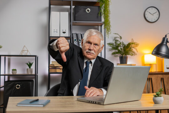 Dislike. Upset senior businessman working on laptop at home office thumbs down sign gesture, expressing discontent, disapproval, dissatisfied bad work. Displeased serious freelancer grandpa in suit. - Powered by Adobe