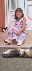 A little caucasian girl playing with small kittens in front of the house
