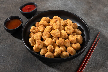 Chicken popcorn in a black bowl with ketchup and sweet chili sauce on a gray background. Appetizer, snack concept.