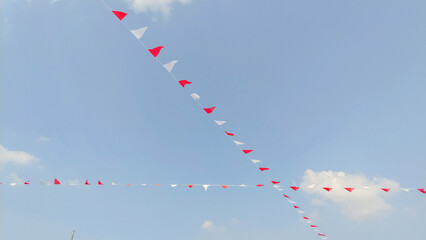 Red and White Bunting Flags Against a Bright Blue Sky with Sparse Clouds