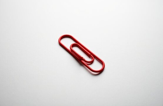 A red paperclip lies on a plain white surface creating a simple minimalist scene