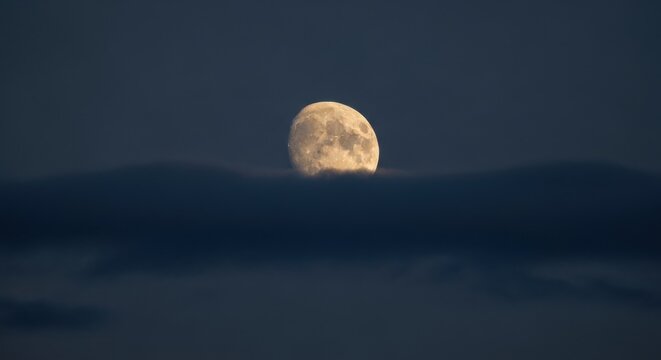 Bright gibbous moon rising over dark clouds. Celestial night sky scene. Astronomy and space exploration concept. Minimalist design with ample copy space for text