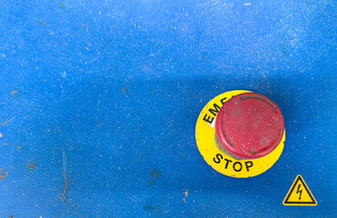 Close-up of a red emergency stop button on a dirty, textured blue industrial control panel.