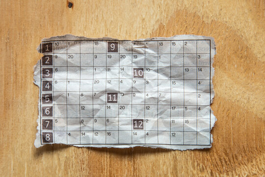 Torn piece of a newspaper puzzle, possibly a number grid or word puzzle, lying on a light brown wooden surface.