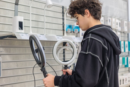 Teenager Choosing Ring Light for Content Creation – Young Blogger Selecting Lighting Equipment in Electronics Store. video recording, streaming, social media content, and vlogging. influencer, Gen Z