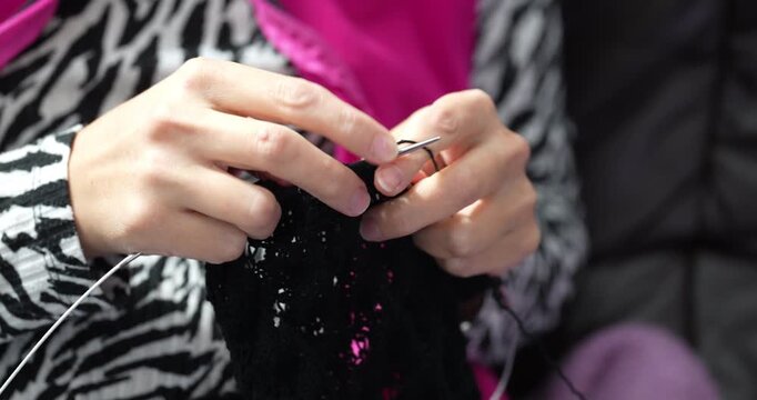 A person sits and carefully works on a knitting project. Black yarn transforms into delicate lace with focused effort and gentle hand movements.