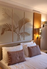 A serene hotel room featuring a three-panel palm leaf artwork above the bed, warm bedside lighting, and plush pillows. The neutral palette creates a calm, inviting space perfect for relaxation.