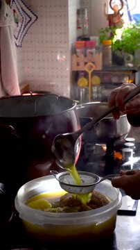 The cook pours the broth over the stew through a strainer