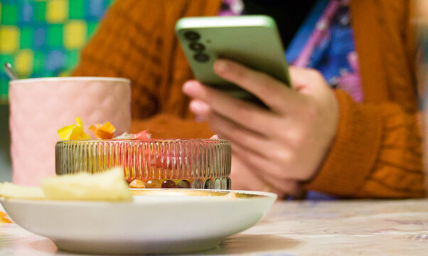 woman using smartphone at breakfast - Scrolling phone while eating - Powered by Adobe
