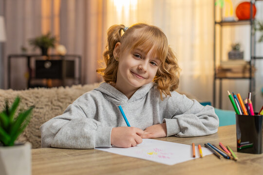 Happy young school girl arranging colorful pencils on table, drawing picture with care. Caucasian 9 years old child kid smiling as admires the result, feeling proud of her work and expressing joy