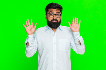 Indian man shrugs shoulders raises open palms expressing uncertainty or confusion in awkward moment. Arabian guy isolated on green chroma key background showing emotional gesture of not knowing answer