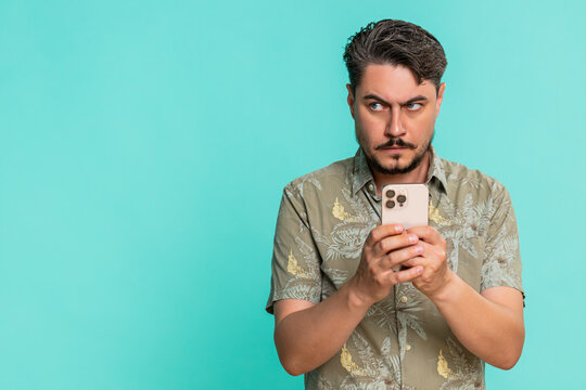 Middle-aged man anxiously types fast on smartphone, breathing deeply while focused on composing urgent message. Young adult guy on blue background shows tension, nervousness, digital communication.