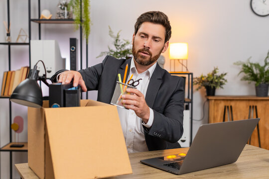 Middle-aged businessman at home office packs items carefully into box and glances around with nostalgia. Freelancer guy at table labels box closes notebook and smiles ready for next step in move soon.