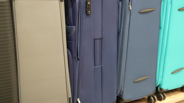 Various suitcases are shown in a row at a store. Colors include blue, grey, teal, black, and red. They are lined up and ready for purchase for your next trip.