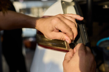 Hands fixing car light, Closeup of hands replacing taillight under open trunk lid, Individuals collaboratively repairing electrical wiring for vehicle tail light assembly