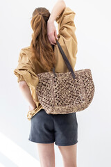 Elegant woman in beige windbreaker jacket and black shorts on light background. Fashionable female style. Studio photography. Vertical photo. Back view