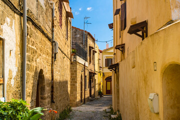 Fototapeta premium Narrow cobblestone alley with yellow stone walls in the Rhodes Old town, Greece