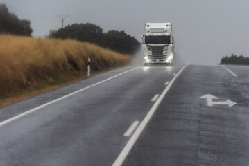 Truck cresting a hill on a rainy road under a dark stormy sky, front view with water spray