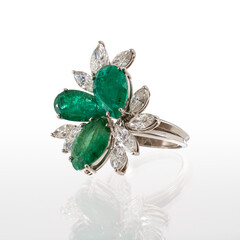 platinum ring with two pear-cut emeralds and one marquise-cut emerald surrounded by nine diamond navettes, isolated on white background