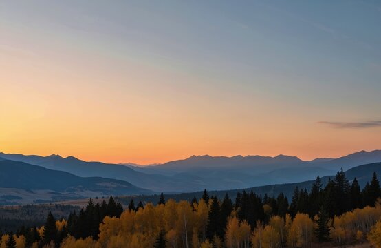 Sunset over Colorado Rocky Mountains. Mountain range with hills, trees in foreground. Orange, yellow sky with clouds at dusk. Natural landscape with evergreen, yellow trees. Scenic view of mountains - Powered by Adobe