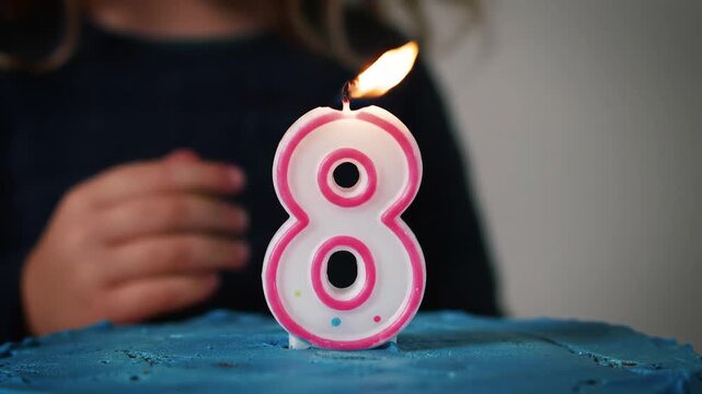 Closeup of a childs hands preparing to blow out a lit number eight birthday candle on a cake celebrating an eighth birthday with joy and anticipation.