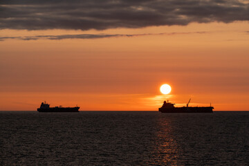 Fototapeta premium Two cargo ship silhouettes on the Baltic Sea horizon during a beautiful orange sunset off the coast of Estonia.