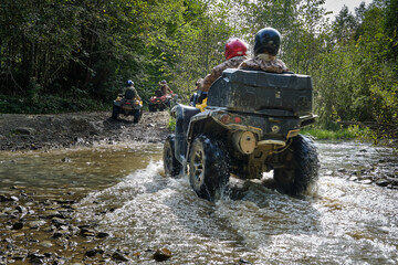 Adventure trip on a quad bike. Group of people riding ATVs through a muddy forest path and a stream. © Volodymyr