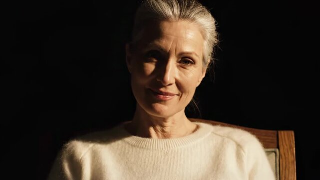 Mature woman reading a book in a dimly lit room, enjoying a quiet moment of reflection and learning.