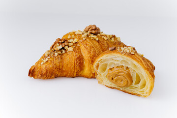 Flaky croissant filled with caramel cream and topped with walnuts on white background