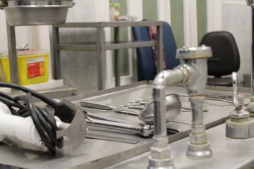 Mesa de disección de acero inoxidable con instrumental quirúrgico y grifos en primer plano, sala de autopsias o laboratorio de anatomía y patología