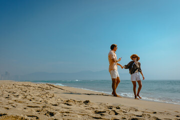 Young caucasian couple walking on sandy beach under clear sky