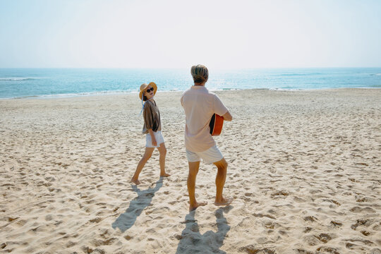 Young caucasian couple enjoys beach walk with guitar on sunny day - Powered by Adobe