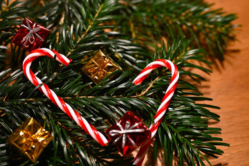 Close-up of red and white candy canes forming a heart shape on green fir branches, surrounded by small golden and red presents. Cozy and festive Christmas decoration