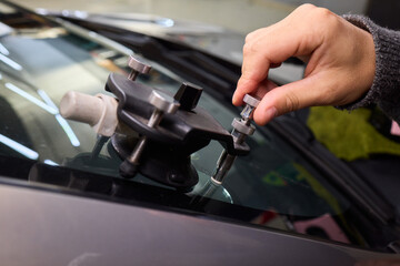 Closeup of technician repairing windshield inside garage, Professional technician employs specialized equipment to mend damaged windshield efficiently and safely