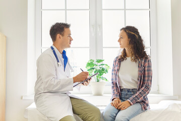 Fototapeta premium Doctor and woman patient during clinic consultation checkup. Friendly physician reviews appointment history, diagnosis, and wellness, providing healthcare. Medical care, medicine and support.