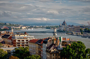 Naklejka premium Budapest, Hungary - July 28, 2025: Panoramic view of the Danube River flowing through central Budapest, with the Hungarian Parliament Building visible on the right and city architecture lining the riv