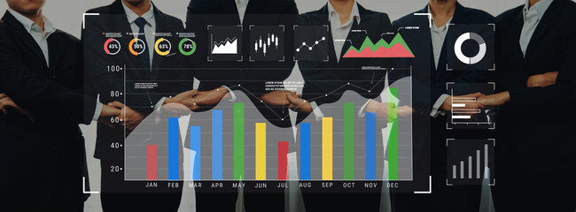 A professional team in business attire stands together, analyzing data trends displayed on modern graphs, emphasizing collaboration and strategy development in a corporate environment. Trope