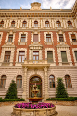 Obraz premium Budapest, Hungary – July 27, 2025: Colorful residential buildings with ornate balconies and street-level shops in downtown Pest, capturing the city’s architectural charm and everyday urban life. 