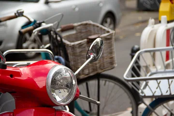 Selbstklebende Fototapeten Roller Red scooter parked on city street, showcasing chrome details and vintage design, surrounded by bicycles and urban elements, capturing vibrant city life and transportation culture  © Yahor