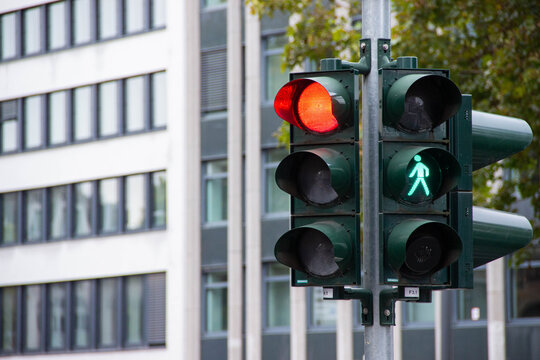 Traffic light displaying red and green signals for vehicles and pedestrians, positioned on a street corner, with modern buildings in the background, illustrating urban traffic management