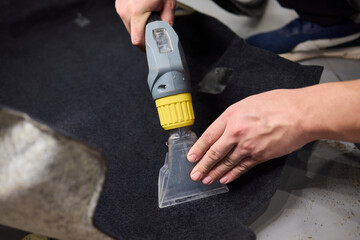 Automotive cleaning process, Professional vehicle upholstery maintenance and dirt removal, Detailed view of cleaning device removing grime from dark fabric upholstery