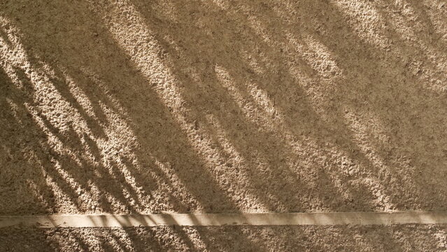 A natural, textured, beige stone or concrete wall background with harsh diagonal shadows and a subtle crack detail, perfect for graphic design overlays or architectural backdrops.