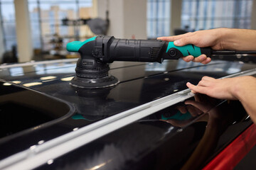 Polishing black car surface thoroughly, Detailed buffing to achieve showroom quality shine, Expert technician uses orbital buffer and foam pad to enhance vehicle gloss