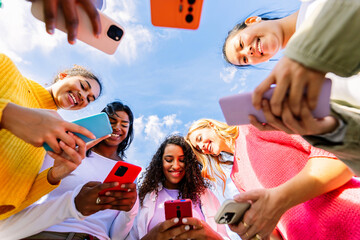 Multiracial women smiling while using smartphones outdoors. Young female friends connected through technology and social media. Digital lifestyle and community concept.
