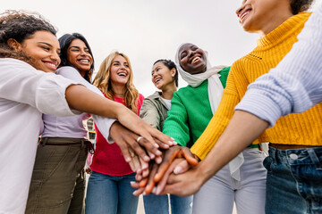 Group of diverse women stacking hands outdoors. Joyful friends expressing unity, teamwork and empowerment. Community and togetherness concept.
