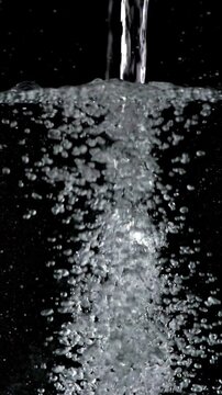 Vertical video of water pouring and filling a container. Slow motion.