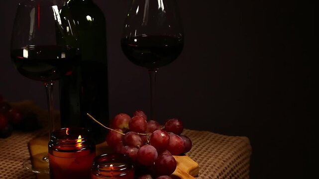 Still life two wine glasses with grapes bunch near romantic aroma burning flame fire candles on a table on dark backround. Decor concept of Christmas holiday celebration with fresh sweet ripe dessert
