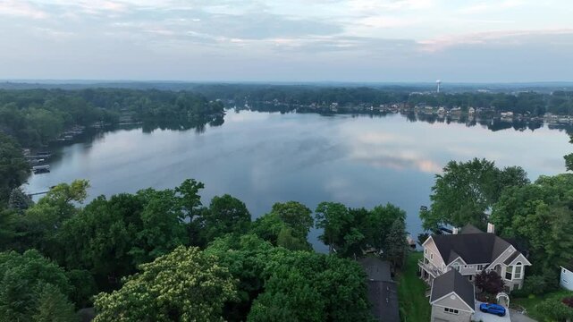 Aerial 4K of a calm lakeside community at early morning under semi-cloudy skies&mdash;glassy water, lush trees, and waterfront homes; perfect for travel, real estate, and lifestyle b-roll.