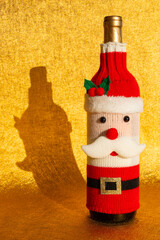 a wine bottle dressed in a festive Santa Claus-themed knitted cover on golden background at vertical composition